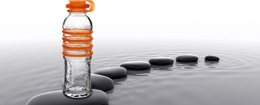 A orange glass water bottle is seen perched on rocks in water
